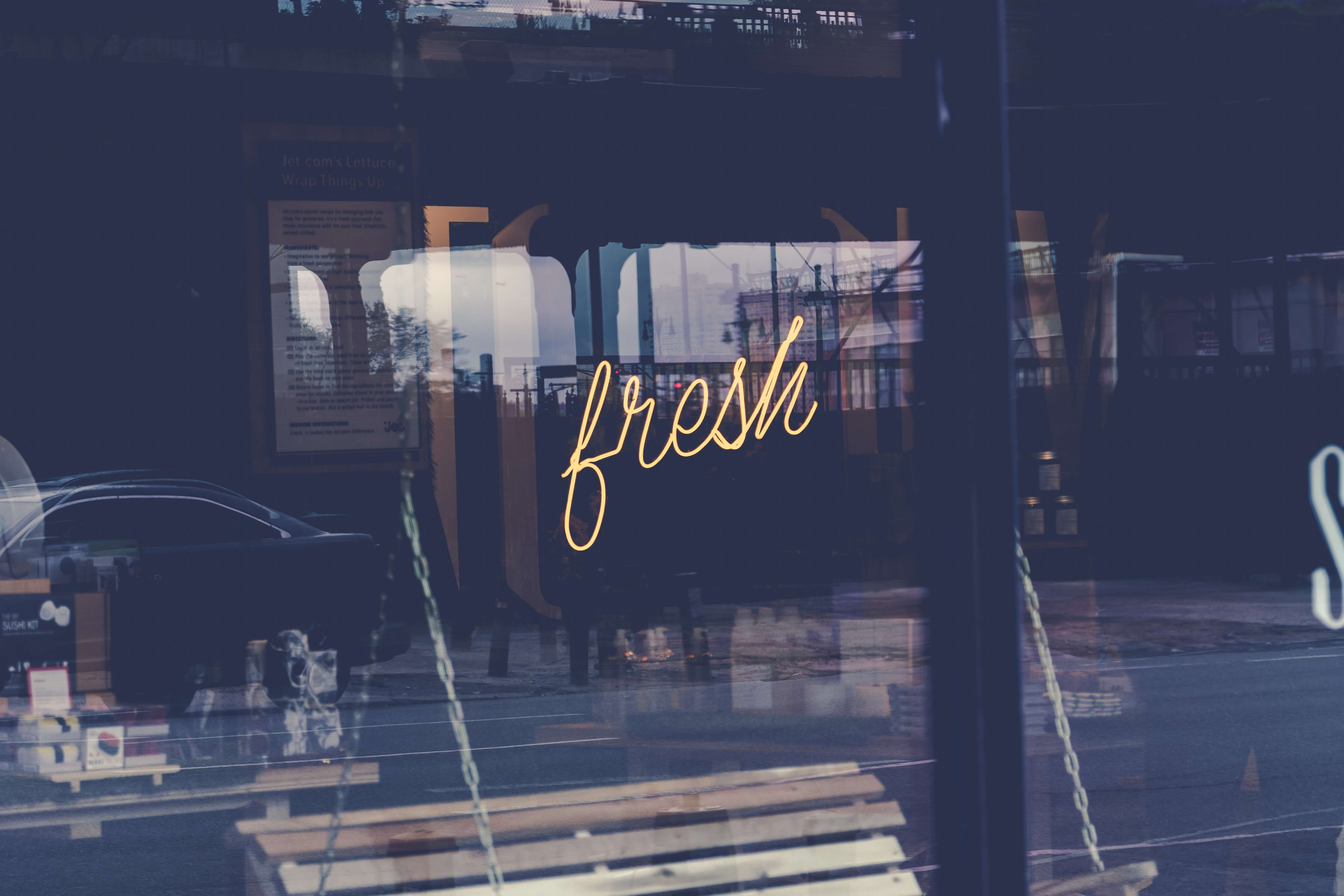 A storefront sign on a window reading fresh stands out against dark glass and reflections.